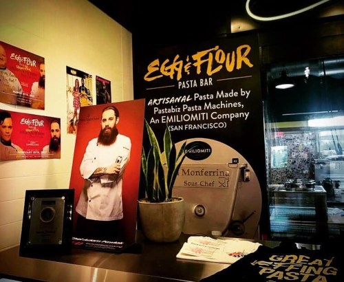 A pasta bar display featuring a chef, pasta machine, and promotional materials for Egg & Flour in San Francisco.