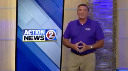 A news anchor in a purple shirt stands in front of a news set with the "Action News 2" logo displayed.