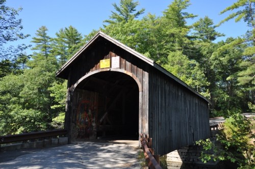 A wooden covered bridge surrounded by lush green trees under a clear blue sky.