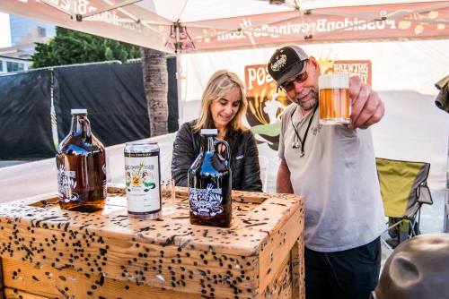 A woman and a man at a craft beer booth, with bottles and a can on display, enjoying a drink together.