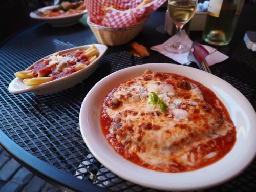 A plate of cheesy lasagna in marinara sauce, with a side of pasta, on a black metal table.