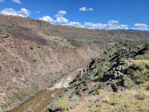 A scenic view of a river winding through a rocky canyon under a blue sky with scattered clouds.