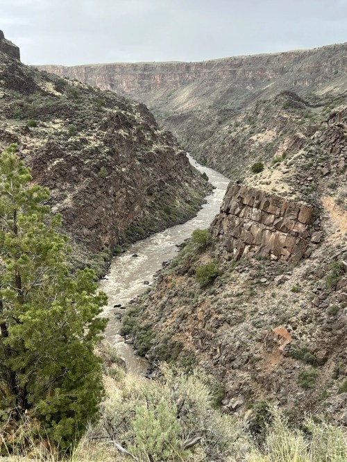 A winding river flows through a rugged canyon, surrounded by rocky cliffs and sparse vegetation.