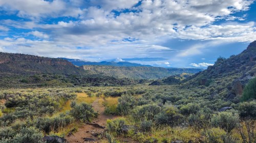 A scenic landscape featuring rolling hills, green shrubs, and a blue sky with scattered clouds.