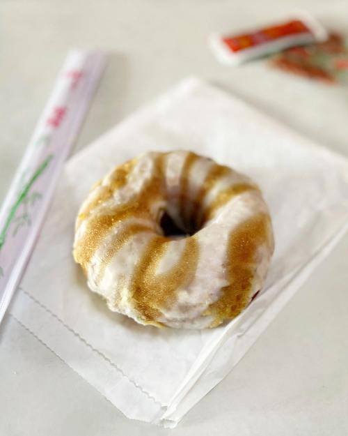 A glazed donut with a swirl pattern, resting on a white paper napkin, with a straw and condiment packet in the background.