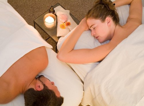 A couple enjoying a relaxing side-by-side massage in a serene spa setting with candles and soft towels.