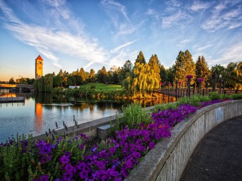 A scenic park with vibrant flowers, a calm lake, and a clock tower under a blue sky with wispy clouds.