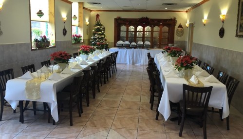 A festive dining room with two long tables set for a meal, decorated with poinsettias and a Christmas tree in the corner.
