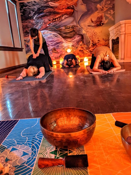 A serene yoga studio with people practicing poses, surrounded by salt lamps and singing bowls on colorful mats.