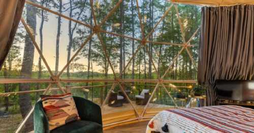 Cozy interior of a geodesic dome with large windows showcasing a forest view at sunset.