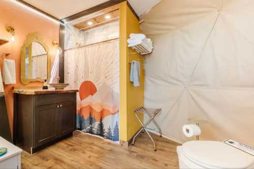 A modern bathroom featuring a shower with a mountain sunset curtain, a dark vanity, and warm lighting.