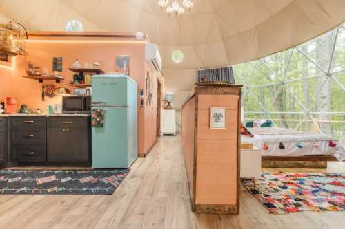 Cozy interior of a geodesic dome featuring a kitchen, bed, and colorful decor, surrounded by nature.