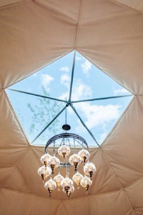 A chandelier hangs from a geometric ceiling with a skylight, revealing blue skies and clouds above.