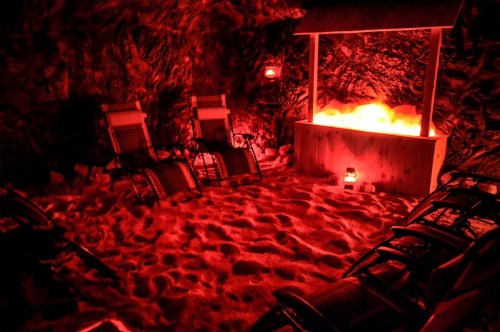 A dimly lit salt room with red lighting, featuring lounge chairs and a glowing salt display.