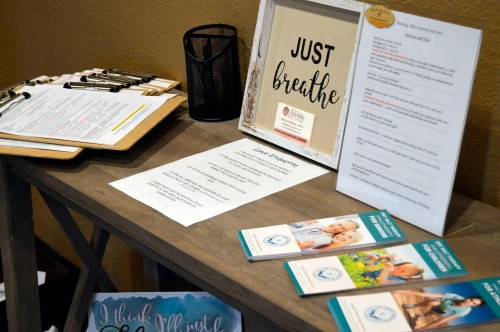 A table displaying informational brochures, a framed sign saying "Just breathe," and various printed materials.