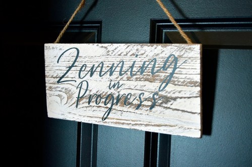A wooden sign hanging on a door reads "Zoning in Progress" in decorative lettering.