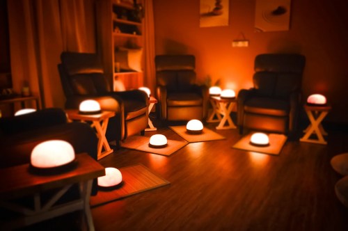 A cozy room with dim lighting, featuring several glowing lamps and comfortable chairs arranged for relaxation.