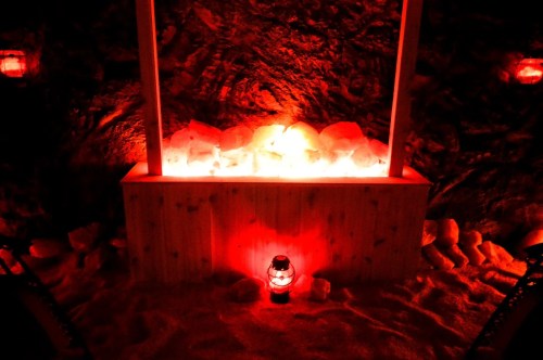 A dimly lit room with a wooden box filled with glowing red salt, surrounded by lanterns and a sandy floor.