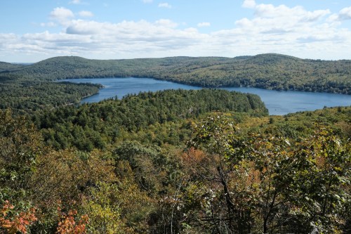A scenic view of a lake surrounded by lush green hills and trees under a partly cloudy sky.
