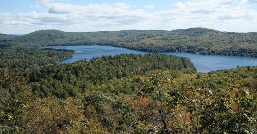 A scenic view of a lake surrounded by lush green hills and trees under a partly cloudy sky.