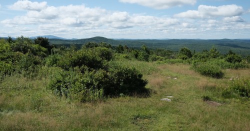 A scenic view of rolling hills and lush greenery under a partly cloudy sky.