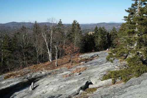 A rocky landscape with sparse trees and distant mountains under a clear blue sky.