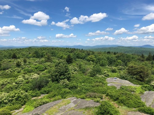 A panoramic view of lush green hills under a blue sky with fluffy white clouds.