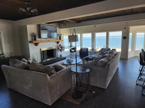 Bright, modern living room with a large sofa, coffee table, and a view of the water through large windows.