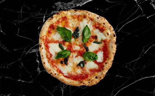 A freshly baked Margherita pizza topped with mozzarella cheese and fresh basil on a black marble background.