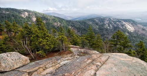 A scenic view of mountains and forests from a rocky overlook, with misty hills in the background.