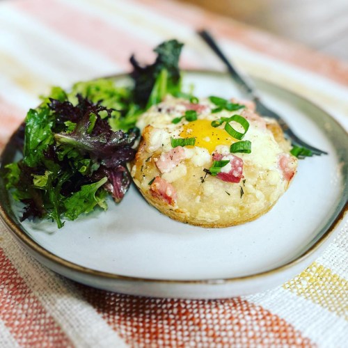 A plate with a baked egg dish topped with green onions, served alongside a fresh mixed green salad.