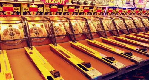 A row of illuminated skee-ball machines in a vibrant arcade setting.