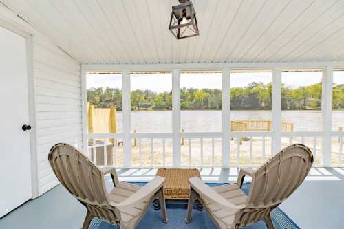 Cozy porch with two chairs and a table, overlooking a serene lake surrounded by greenery.