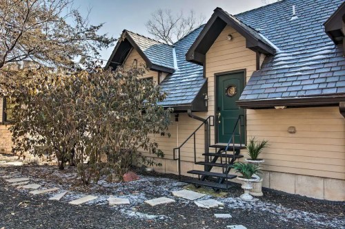 A cozy house entrance with a green door, stone steps, and a landscaped garden, lightly dusted with snow.