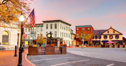 Charming town square at sunset, featuring historic buildings, a clock, and autumn foliage.