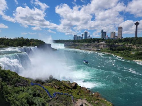 A scenic view of Niagara Falls with mist, a boat on the water, and a skyline of tall buildings in the background.