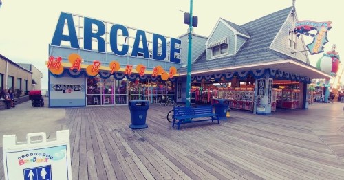 A colorful arcade building with "ARCade" signage, surrounded by wooden boardwalk and game booths.