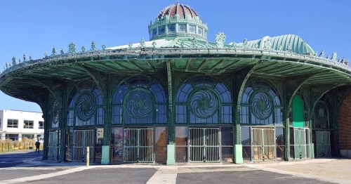 Historic circular building with ornate green metalwork and large windows, set against a clear blue sky.