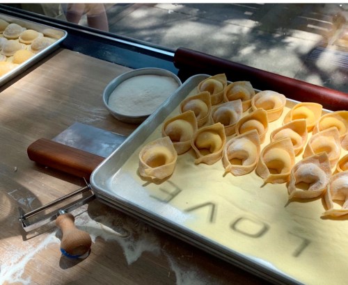 A tray of freshly made dumplings on a wooden surface, with flour and a rolling pin nearby.