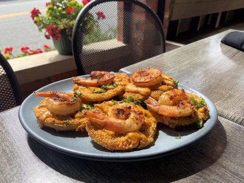 A plate of golden fried shrimp on cornmeal cakes, garnished with herbs, served outdoors with flowers in the background.