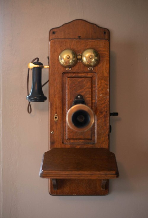 A vintage wooden wall-mounted telephone with brass bells and a black receiver.