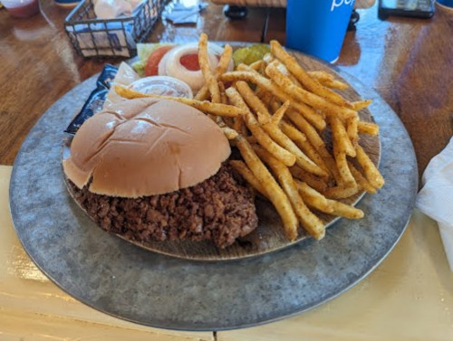 A plate with a fried chicken sandwich, fries, and condiments, set on a wooden table.