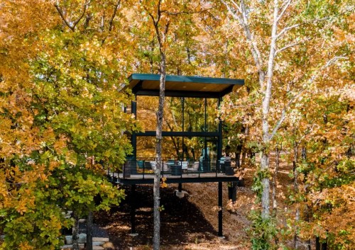Modern treehouse nestled among vibrant autumn foliage, featuring large windows and a deck.