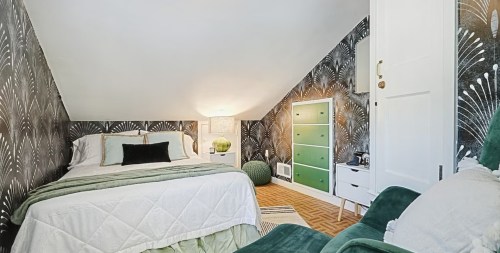 Cozy attic bedroom with patterned wallpaper, a green dresser, and a bed adorned with green and white bedding.