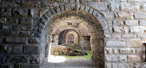 Stone arches lead to a grassy area, framed by weathered brick walls in an old, abandoned structure.