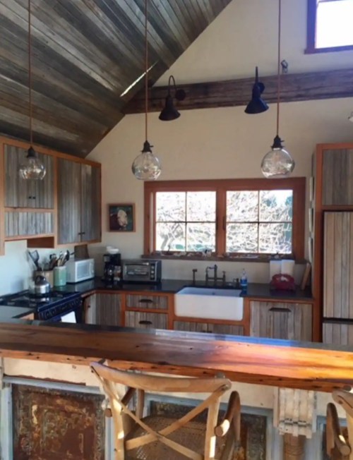 Cozy kitchen with wooden accents, a farmhouse sink, and pendant lights, featuring a rustic design and large windows.