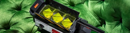 A close-up of a device with three yellow crystals inside, resting on a vibrant green tufted surface.