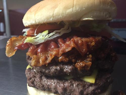 A towering burger with two beef patties, crispy bacon, lettuce, tomato, and cheese, all in a soft bun.
