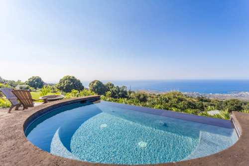 A serene infinity pool overlooking a scenic landscape and ocean under a clear blue sky.