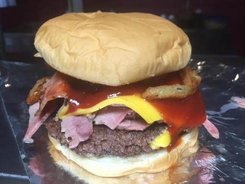 A close-up of a burger with a beef patty, cheese, ham, crispy onions, and barbecue sauce on a soft bun.